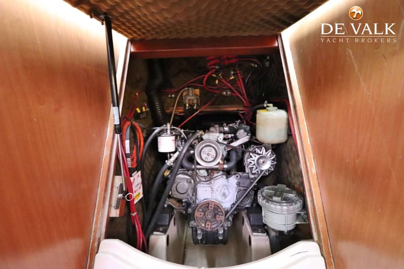 Een motorruimte met een scheepsmotor, diverse slangen, kabels en een expansievat.