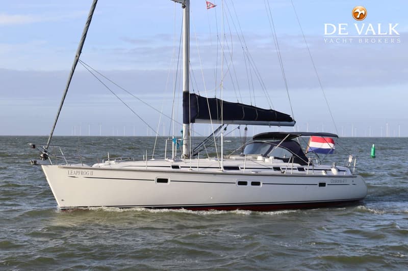 Een witte zeilboot met de naam "LEAPFROG II" en "Océanis 411" vaart op water met windmolens op de achtergrond.