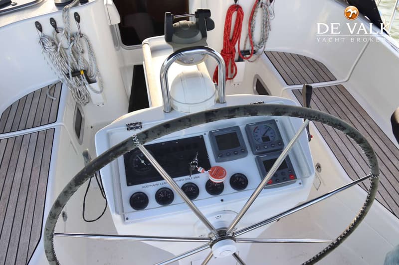 Een stuurwiel met instrumentenpaneel, kompas en touwen op een bootdek.