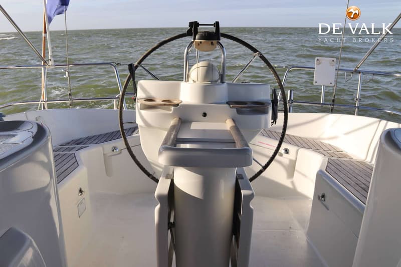 Een witte boot met een stuurwiel en houten zitjes, varend op een water met lichte golven onder een heldere lucht.