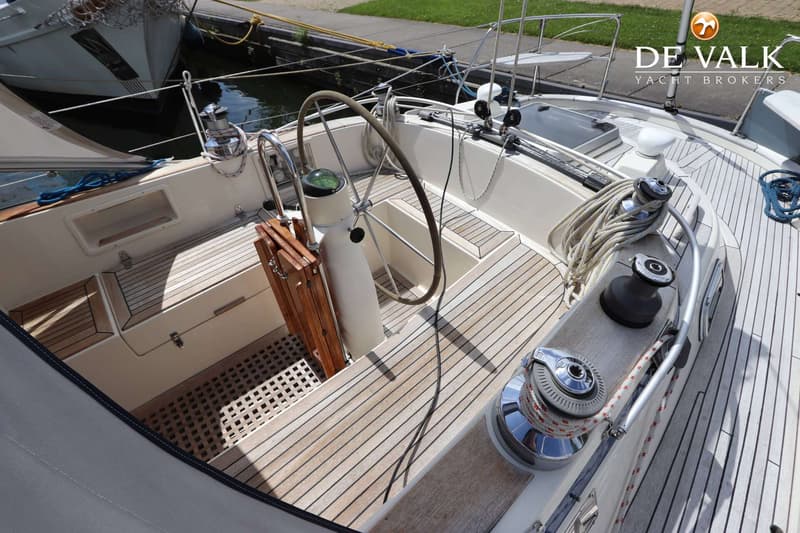 Een bovenaanzicht van de kuip van een zeilboot met een stuurwiel, kompas, houten dek en lieren. — Hallberg Rassy 39