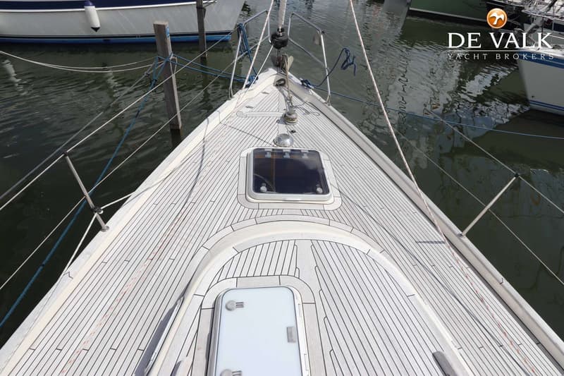 Een bovenaanzicht van het voordek van een zeilboot met een houten dek, luiken en een ankerlier. — Hallberg Rassy 39