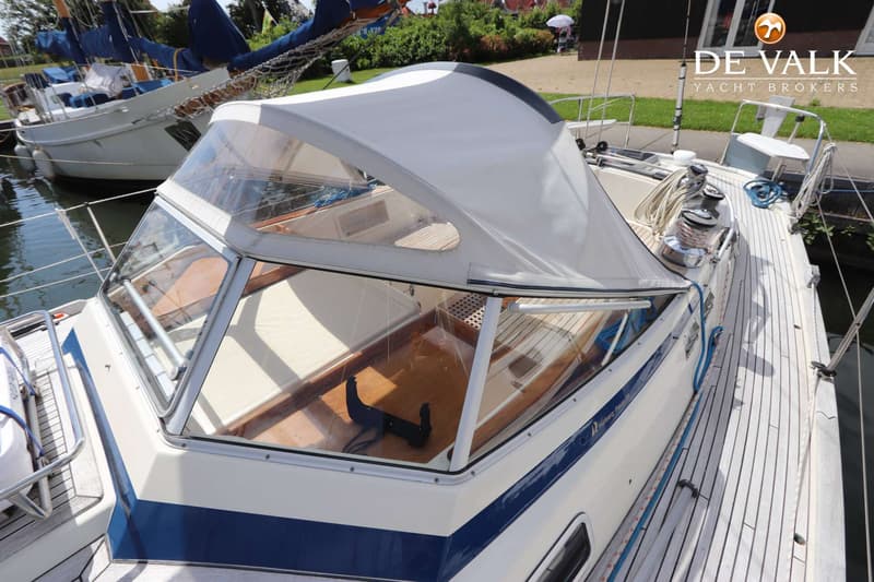 Een witte boot met blauwe strepen en een witte buiskap ligt in het water, met een andere boot op de achtergrond.