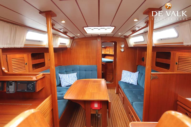 De foto toont het interieur van een boot met houten wanden, een houten tafel en blauwe banken met gestreepte kussens.