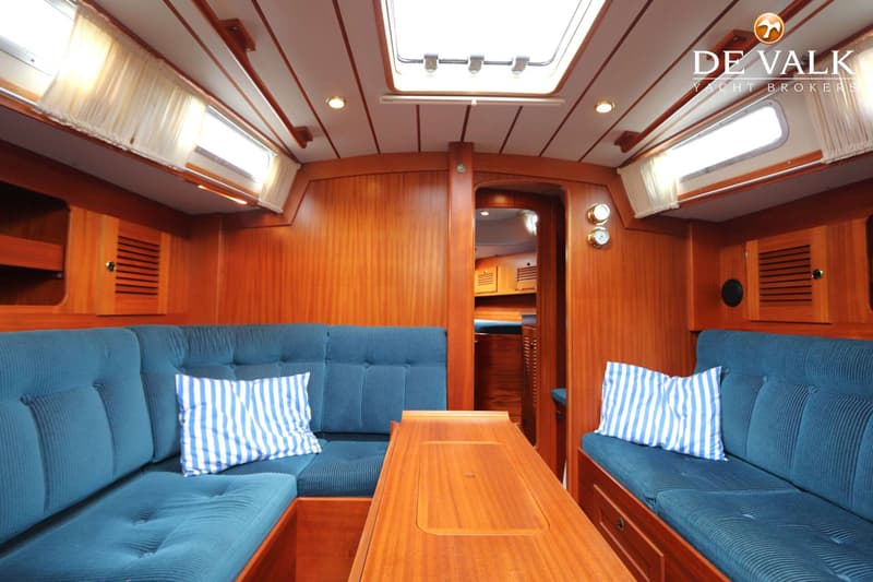 De foto toont het interieur van een boot met houten wanden, blauwe banken, een tafel en een doorkijk naar een andere ruimte.