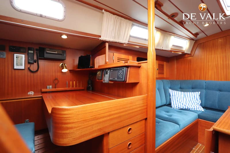 De foto toont een houten interieur van een boot met een blauwe bank, een bureau en diverse navigatie-apparatuur.