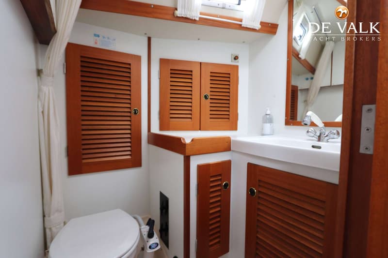 De foto toont een badkamer met een toilet, een wastafel met kraan en spiegel, en houten kastjes met jaloeziedeur.