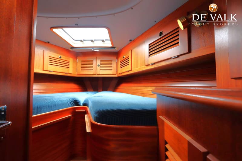 De foto toont een kajuit met twee bedden met blauwe dekens, houten wanden en kasten, en een dakluik. — Hallberg Rassy 39