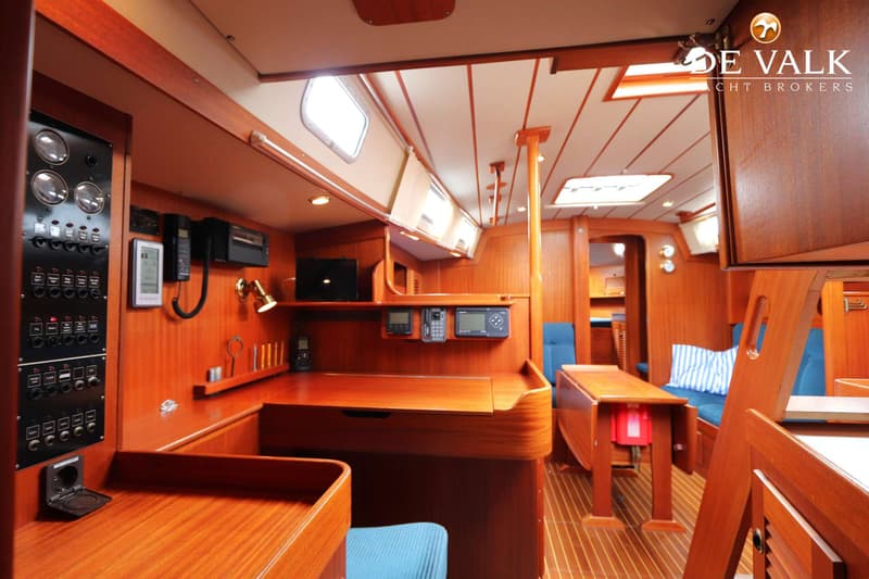 De foto toont het interieur van een boot met houten afwerking, een navigatiehoek en een zithoek met blauwe kussens.