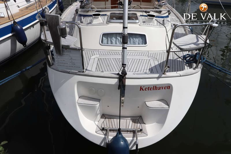 Een witte zeilboot met de naam "Ketelhaven" in rode letters op de spiegel, ligt in het water. — Hallberg Rassy 39