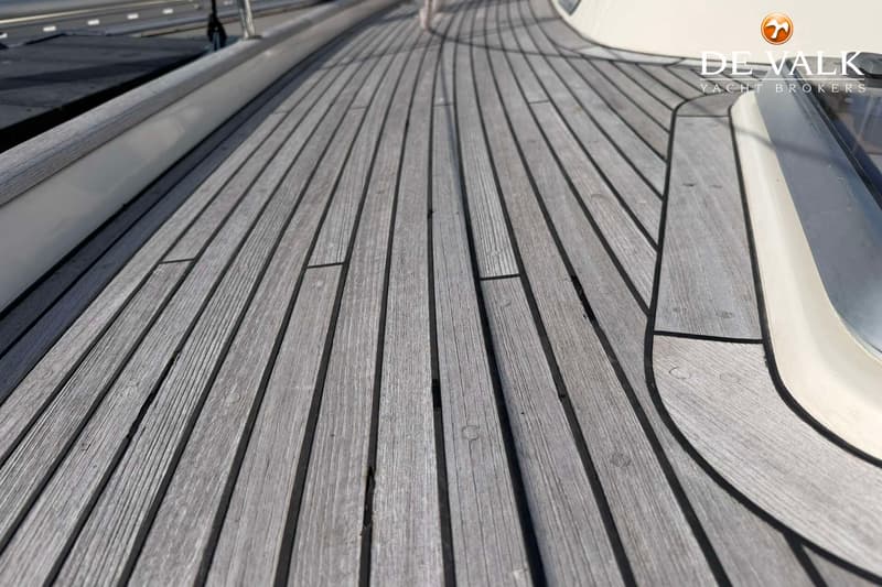 Een close-up van een houten dek met lange, smalle planken en zwarte naden, met een wit boord aan de zijkant.