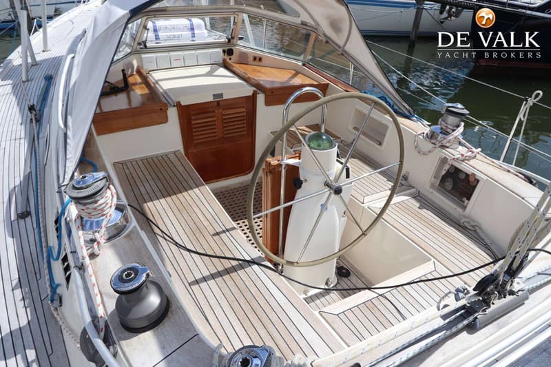 Een bovenaanzicht van de kuip van een zeilboot met een stuurwiel, kompas, lieren en houten dek. — Hallberg Rassy 39