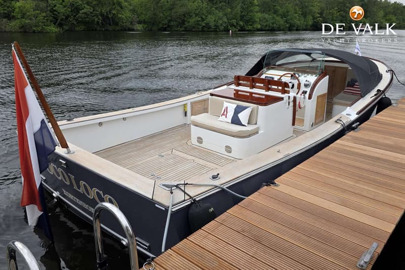 Een donkerblauwe boot met een houten dek en een Nederlandse vlag, afgemeerd aan een houten steiger. — Oak Brothers 29 Lobster