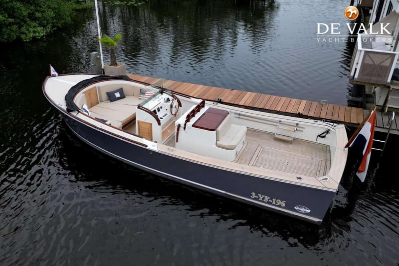 Een donkerblauwe boot met een houten dek en beige kussens ligt aangemeerd aan een houten steiger. — Oak Brothers 29 Lobster