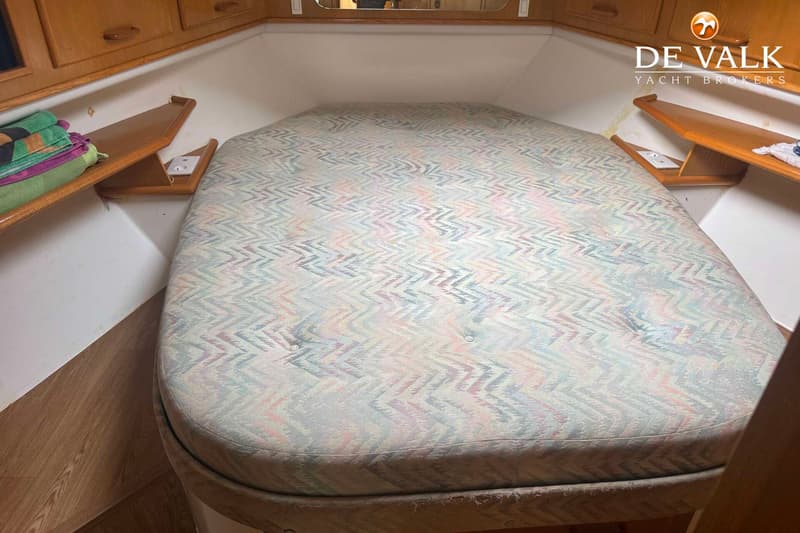 Een kajuit met een groot bed met een zigzagpatroon, houten kasten en planken aan de zijkanten. — Fairline 43