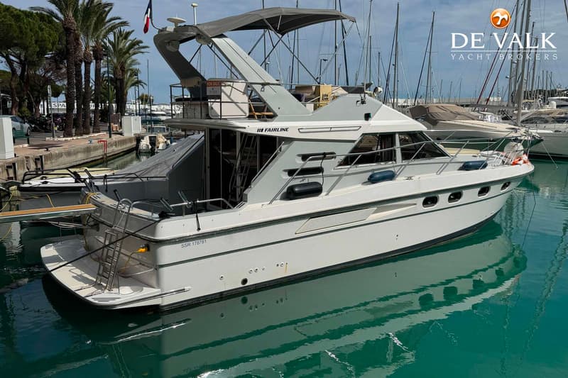 Een witte motorboot met de naam "FAIRLINE" ligt in een haven, omringd door andere boten en palmbomen. — Fairline 43