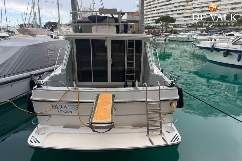 Een witte boot met de naam "PARADIS LONDON" op de spiegel, met een zwemplateau, een zwemtrap en een loopplank. — Fairline 43