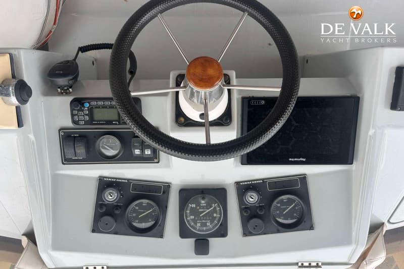 Een stuurwiel met houten middenstuk en diverse meters en bedieningspanelen op een dashboard.