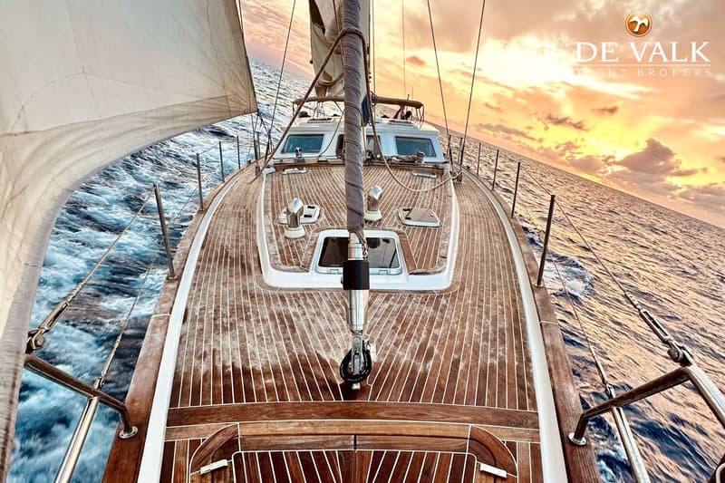 Een zeilboot met een houten dek vaart op zee, met een deels uitgerold zeil en een mast aan de voorzijde. — CRN 63