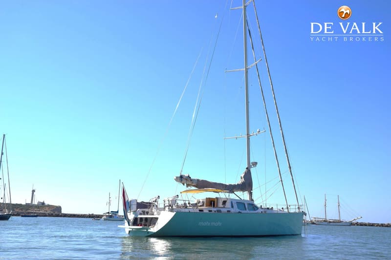 Een lichtblauwe zeilboot met de naam "mahi mahi" op de romp ligt in het water, met een vlag aan de spiegel. — CRN 63