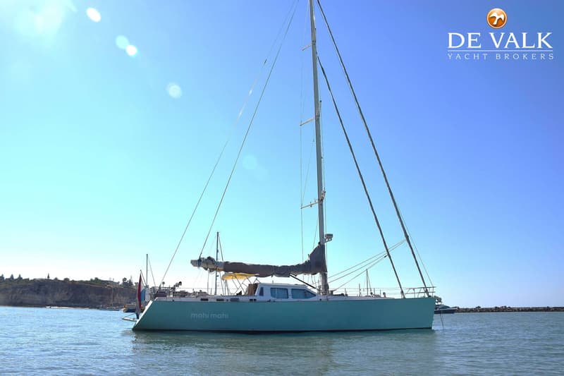 Een lichtblauwe zeilboot met de naam "mahi mahi" op de romp ligt op het water onder een heldere hemel. — CRN 63