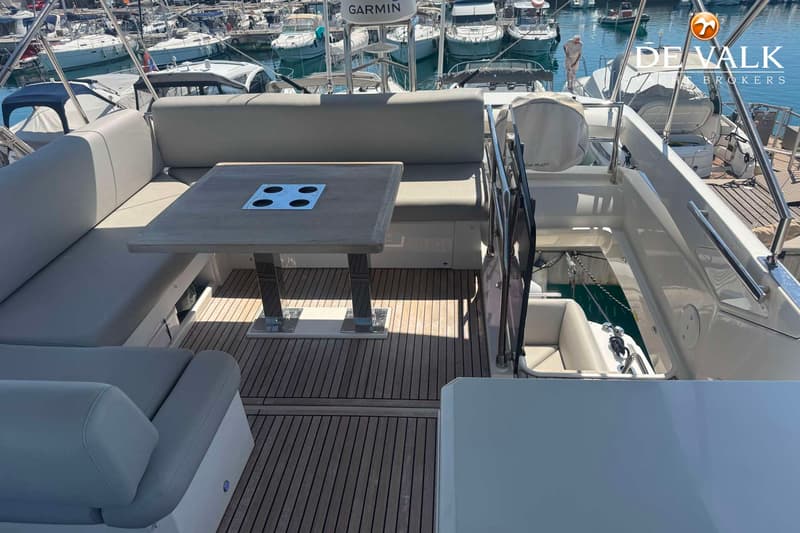 Een bootdek met een houten tafel, grijze banken en een Garmin-apparaat, omringd door andere boten in een haven.