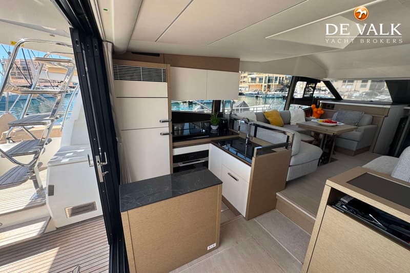 Een interieur van een boot met een keukenblok, een zithoek met tafel en een open schuifdeur naar het achterdek.