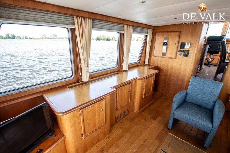 Een interieur van een boot met houten wanden, vloer en meubilair, met uitzicht op water door grote ramen.