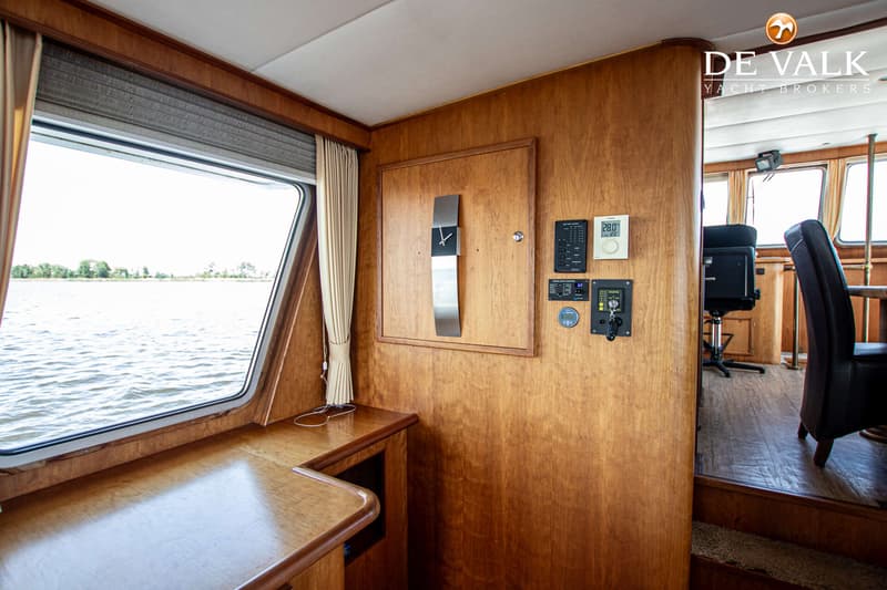 De foto toont een interieur van een boot met houten wanden, een raam met uitzicht op water en een bedieningspaneel.