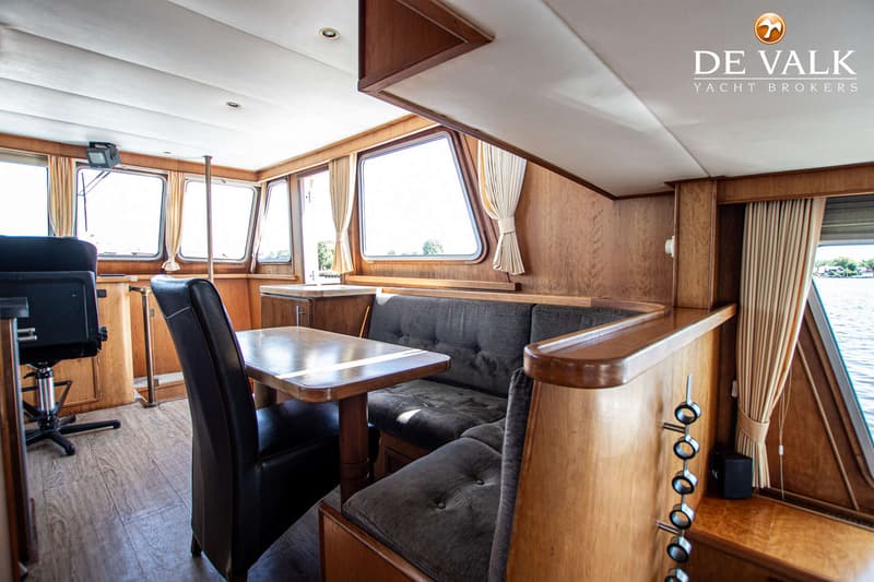 Een interieur van een boot met houten wanden, een tafel met stoelen, een bank en ramen met uitzicht op water.