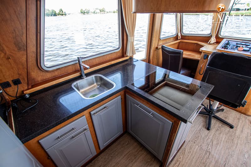 Een kombuis met een spoelbak, inductiekookplaat, donker aanrechtblad en grijze kastjes, met uitzicht op water.