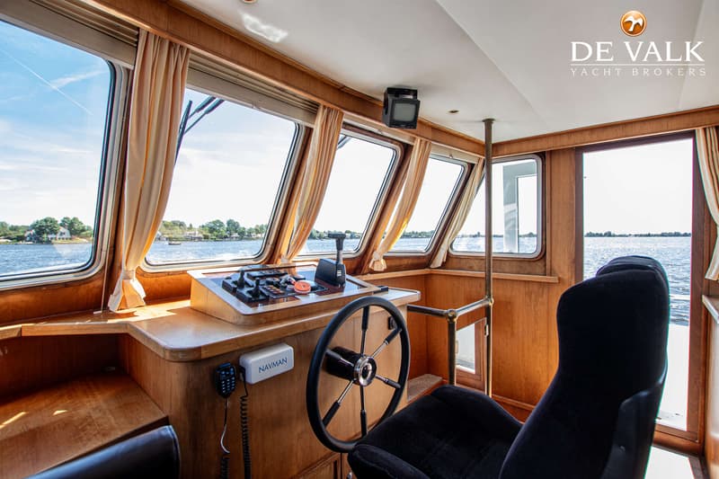 De foto toont de stuurhut van een boot met een stuurwiel, bedieningspaneel, een Navman-apparaat en een zwarte stoel.