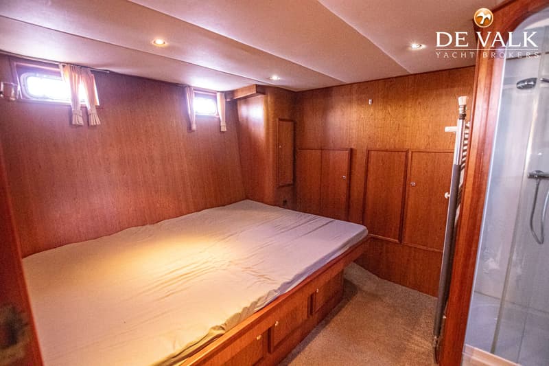 Een slaapkamer in een boot met een bed, twee ramen met gordijnen, houten wanden en kasten, en een douchecabine.