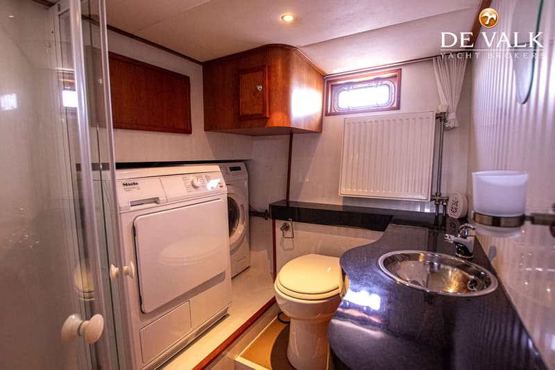 Een badkamer met een wasmachine, droger, toilet, wastafel, radiator en een patrijspoort.