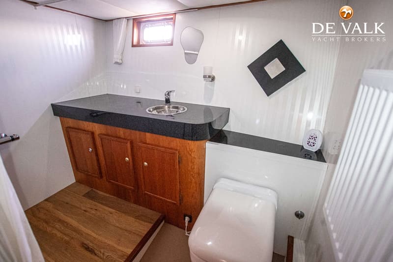 Een badkamer met een wastafel, toilet, spiegel, raam en houten vloer.