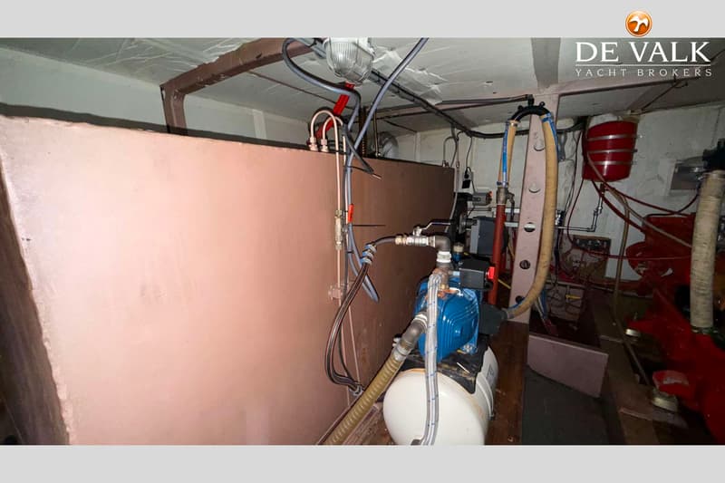 Een machinekamer met een blauwe waterpomp, leidingen, slangen, een rode tank en een roze wand.
