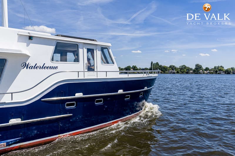 Een blauw-witte boot met de naam "Waterleeuw" vaart op een waterweg onder een blauwe lucht met wolken.