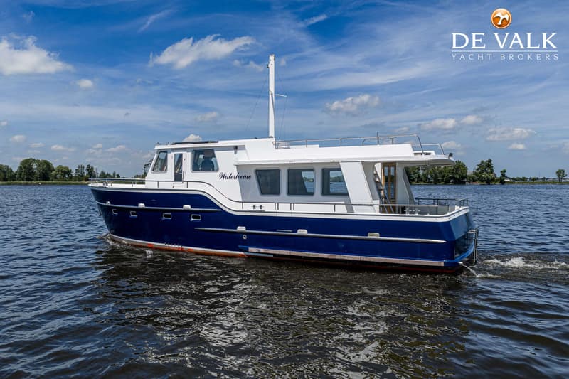 Een blauw-witte motorboot met de naam "Waterleeuw" vaart op een waterweg onder een blauwe hemel met wolken.