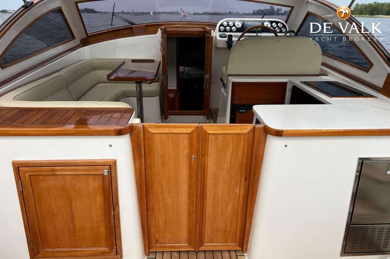 Een interieur van een boot met een stuurstand, een zithoek, een tafel en een kajuitingang. — Long Island 40 Runabout