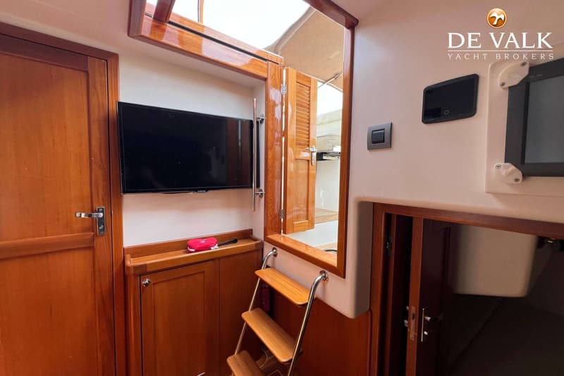Een interieur van een boot met houten deuren, een televisie, een trapje en een open luik naar buiten.