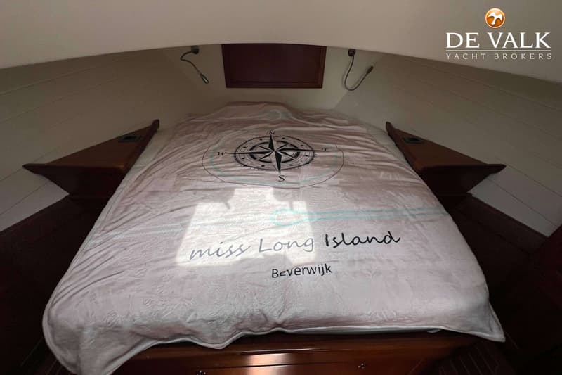 Een bed in een kajuit met een dekbedovertrek met een kompasroos en de tekst "miss Long Island Beverwijk".