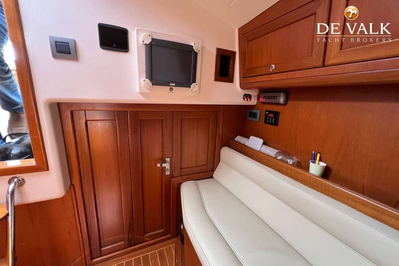 De foto toont een interieur van een boot met houten kasten, een bank met lichte kussens, en diverse bedieningspanelen.