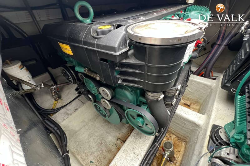 Een close-up van een scheepsmotor met een zwarte behuizing en groene onderdelen, riemen en poelies.