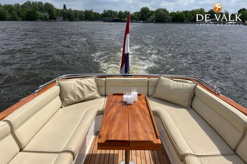 Een boot met een houten tafel, crèmekleurige kussens en een Nederlandse vlag vaart op het water. — Long Island 40 Runabout