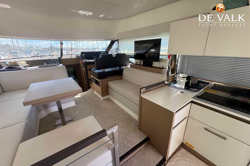 De foto toont het interieur van een boot met een zithoek, tafel, stuurstand, keukenblok en een televisie.
