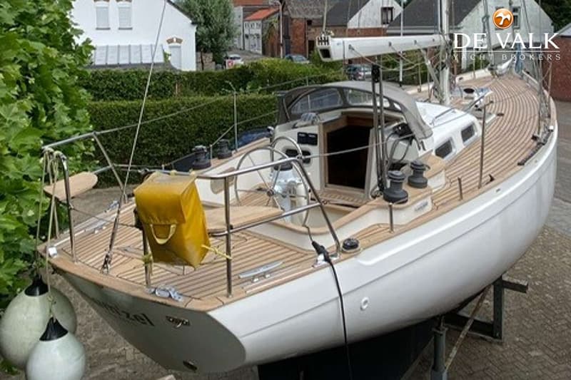 Een witte zeilboot met een teakhouten dek staat op bokken, met een geel zeil en twee stootwillen. — Tradewind 35