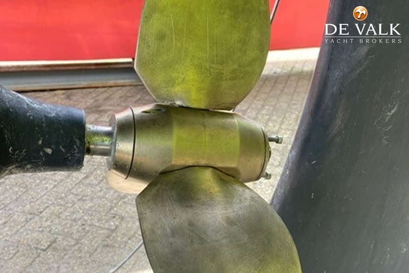 Een close-up van een bronzen scheepsschroef met twee bladen, gemonteerd op een as, met een rood vlak op de achtergrond.
