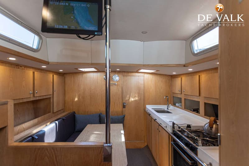 De foto toont het interieur van een boot met een kombuis, zithoek, houten kasten en een navigatiescherm. — Tradewind 35