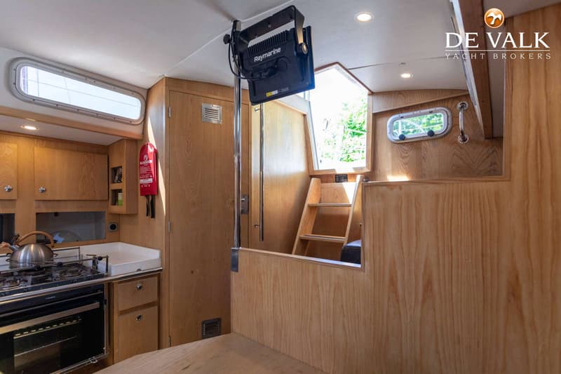 De foto toont een houten interieur van een boot met een kombuis, een trap en een Raymarine-scherm. — Tradewind 35