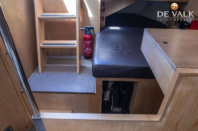 Een interieur van een boot met houten wanden, een trapje, een brandblusser en een donker kussen. — Tradewind 35